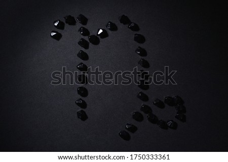 Symbol of the zodiac sign Capricorn made by black stones on a black background. Low dark key. Vignetting lighting. Horoscope Theme
