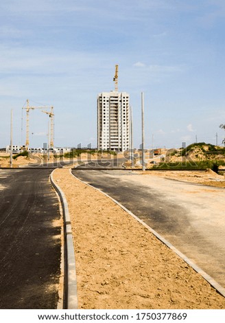 construction cranes on the site of construction of a new residential area, construction of a modern multi-storey building, a new asphalt road was built to the building