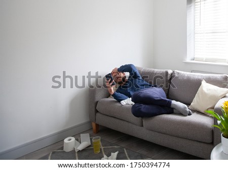 Man Lying Ill on Sofa, Looking at Phone