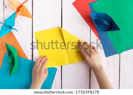 A girl folds colored paper to make origami. A girl makes origami on a wooden table