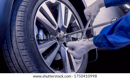 Car repairs. Replacing wheels. Seasonal tire replacement. The master removes the wheel with both hands with the key. A master in uniform. Part of the photo is blurry. Royalty-Free Stock Photo #1750410998