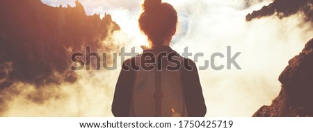 Traveling woman with a backpack standing on a cliff and enjoying landscape and sunset. Wide screen panoramic