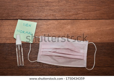 Pink face mask with sanitizer on wooden background. New normal concept image. 