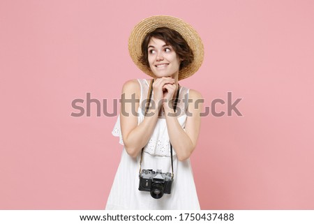 Smiling young tourist woman in summer white dress hat with photo camera isolated on pink background. Female traveling to travel weekends getaway. Air flight journey concept. Put hands prop up on chin