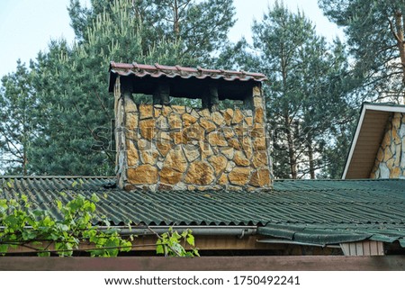 one large brown stone chimney on a green roof on a background of pine trees and sky