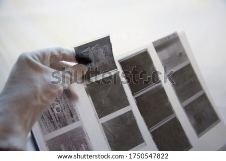 Film photography album for negative storing. A hand with white cotton archival gloves in the background, holding negatives. Different size negatives in special envelopes.