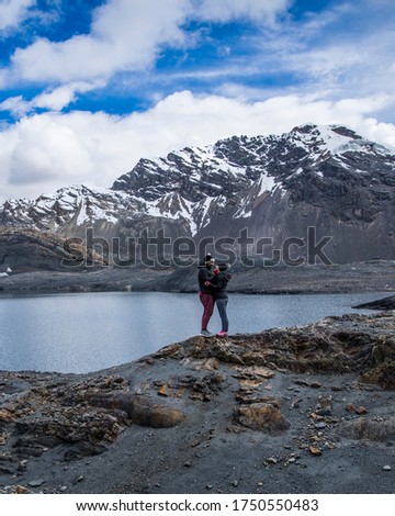 couple in a glacier, near a lake, mountains with snow in their peaks, clouds and blue sky
