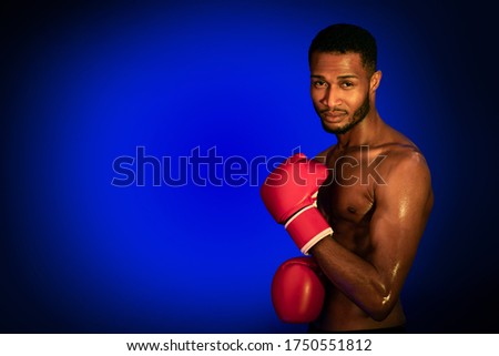 Boxing Concept. Professional Black Boxer Posing Wearing Gloves, Looking At Camera On Blue Studio Background. Copy Space
