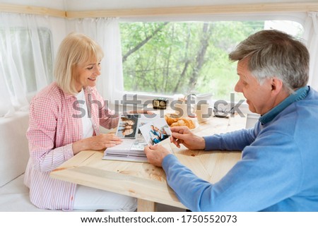 Senior married couple looking through family album with photos inside of their camping vehicle