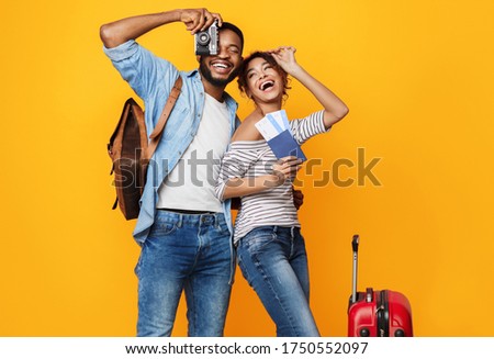 Happy Tourists. Excited African Couple Ready For Vacation, Posing With Suitcase, Tickets And Photo Camera Over Yellow Studio Background.