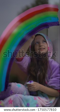 Stay home, flash mob chase the rainbow. girl in pajamas draws the rainbow on the window at home.