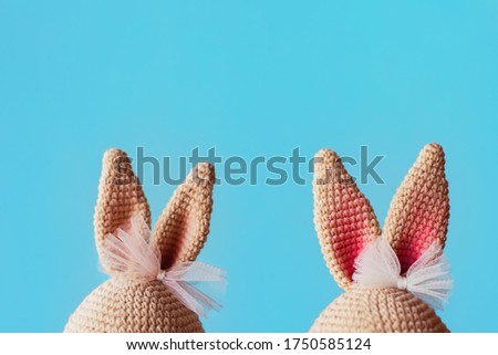 Handmade knitted amigurumi toy. Bunny ears with bows on the blue background. Crochet stuffed animals. 