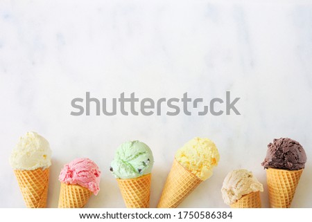 Ice cream cone bottom border with a variety of flavors. Overhead view on a white marble background with copy space.