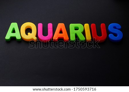 Aquarius text. Zodiac sign written in bright multi-colored cheerful letters on a black dramatic background. Low dark key. Horoscope Theme