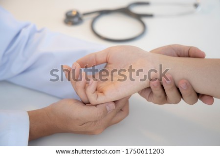 Asian orthopaedic doctor doing physical examination in the patient with wrist pain and numbness at the clinic. Selective focus at right hand. Medical concept