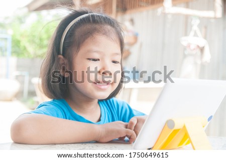 Smiling or Happy Asian Girl learning online course or playing game online on Digital Wireless Device or Tablet at home as Technology e-learning concept.