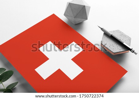 Switzerland flag on minimalist paper background. National invitation letter with stylish pen on stone. Communication concept.