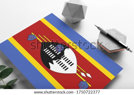 Swaziland flag on minimalist paper background. National invitation letter with stylish pen on stone. Communication concept.