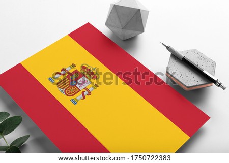 Spain flag on minimalist paper background. National invitation letter with stylish pen on stone. Communication concept.