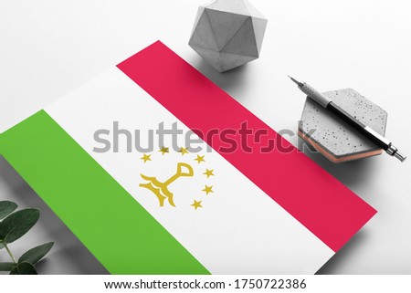Tajikistan flag on minimalist paper background. National invitation letter with stylish pen on stone. Communication concept.
