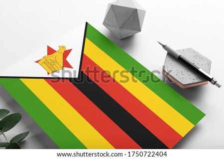 Zimbabwe flag on minimalist paper background. National invitation letter with stylish pen on stone. Communication concept.