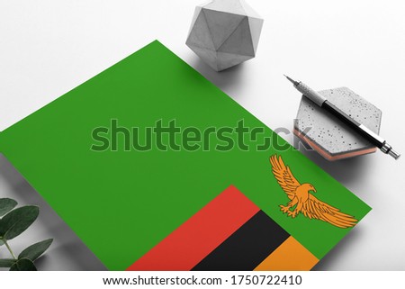 Zambia flag on minimalist paper background. National invitation letter with stylish pen on stone. Communication concept.