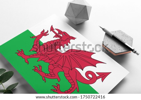 Wales flag on minimalist paper background. National invitation letter with stylish pen on stone. Communication concept.