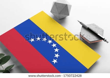 Venezuela flag on minimalist paper background. National invitation letter with stylish pen on stone. Communication concept.