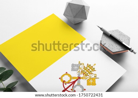 Vatican City flag on minimalist paper background. National invitation letter with stylish pen on stone. Communication concept.