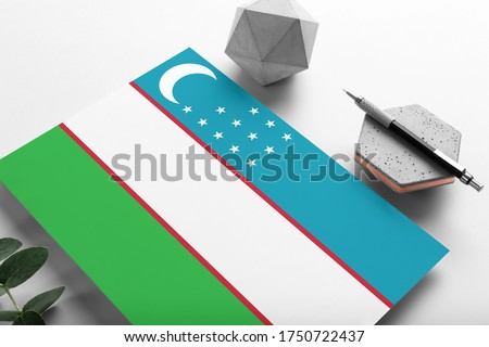 Uzbekistan flag on minimalist paper background. National invitation letter with stylish pen on stone. Communication concept.