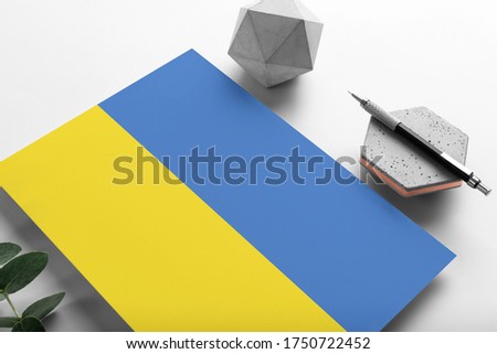 Ukraine flag on minimalist paper background. National invitation letter with stylish pen on stone. Communication concept.