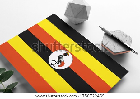 Uganda flag on minimalist paper background. National invitation letter with stylish pen on stone. Communication concept.