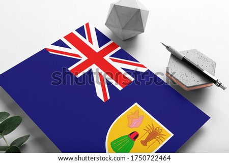 Turks And Caicos Islands flag on minimalist paper background. National invitation letter with stylish pen on stone. Communication concept.