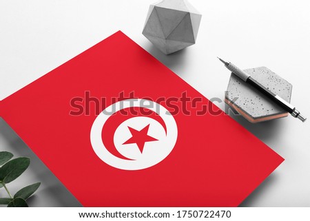 Tunisia flag on minimalist paper background. National invitation letter with stylish pen on stone. Communication concept.