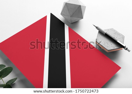Trinidad And Tobago flag on minimalist paper background. National invitation letter with stylish pen on stone. Communication concept.