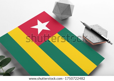 Togo flag on minimalist paper background. National invitation letter with stylish pen on stone. Communication concept.