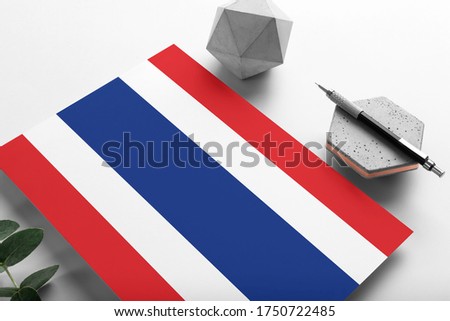Thailand flag on minimalist paper background. National invitation letter with stylish pen on stone. Communication concept.
