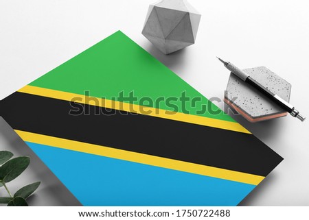 Tanzania flag on minimalist paper background. National invitation letter with stylish pen on stone. Communication concept.