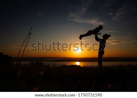 Silhouette of mother and baby raising baby in the air during beautiful sunset on lake background