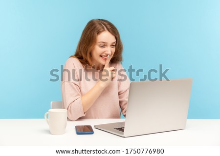 Please, keep secret. Positive young woman in casual clothes shushing with silence gesture, talking on video call, having online communication via laptop at home office. indoor studio shot isolated