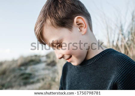 autistic boy sitting in sand dunes looking down shy Royalty-Free Stock Photo #1750798781