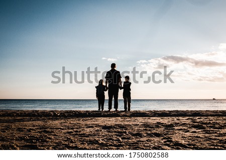 father holding hands with son and daughter looking at the water while standing on the beach Royalty-Free Stock Photo #1750802588