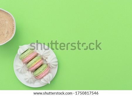 The cup of cappuccino and delicious macarons with white merengues on white plate  on green background. Happy day, breakfast, good morning concepts. Greeting card. Flat lay style with copy space.