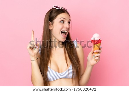 Young caucasian woman in swimsuit holding a cornet ice cream isolated on pink background intending to realizes the solution while lifting a finger up