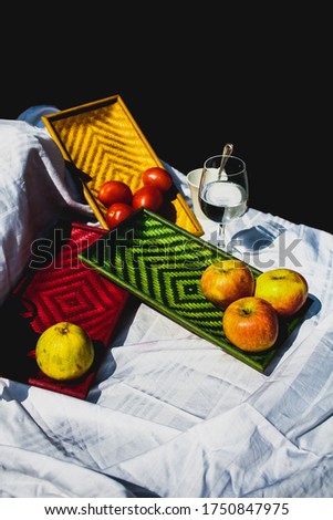 Still life of apples, pear and tomatoes kept on colorful exquisite bamboo trays displayed on a white sheet.