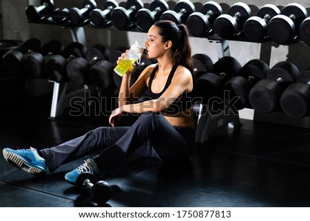 Female athlete taking rest and drinking woter after exercising at gym. Fitness Healthy lifestye and workout at gym concept.