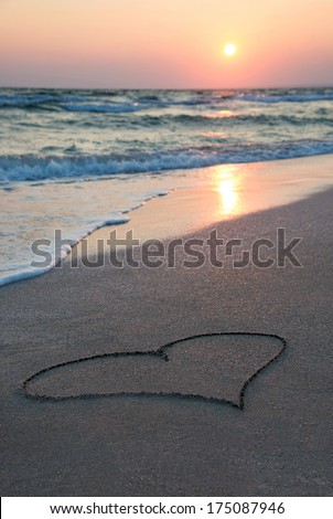 heart outline on wet beach sand against sea wave and sunset