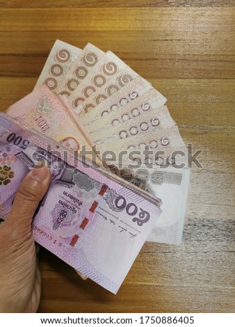 Thai bank note in hand Resting on a wooden table to Performing, giving money or receiving money from Financial institutions, savings, general business exchanged from work or borrowing
