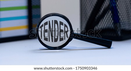 Magnifying glass with the inscription TENDER on a white table. Finance concept.