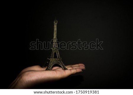 Miniature of Eiffel tower placed on a palm in a black background, design concept can be used in blogs,wallpaper designs